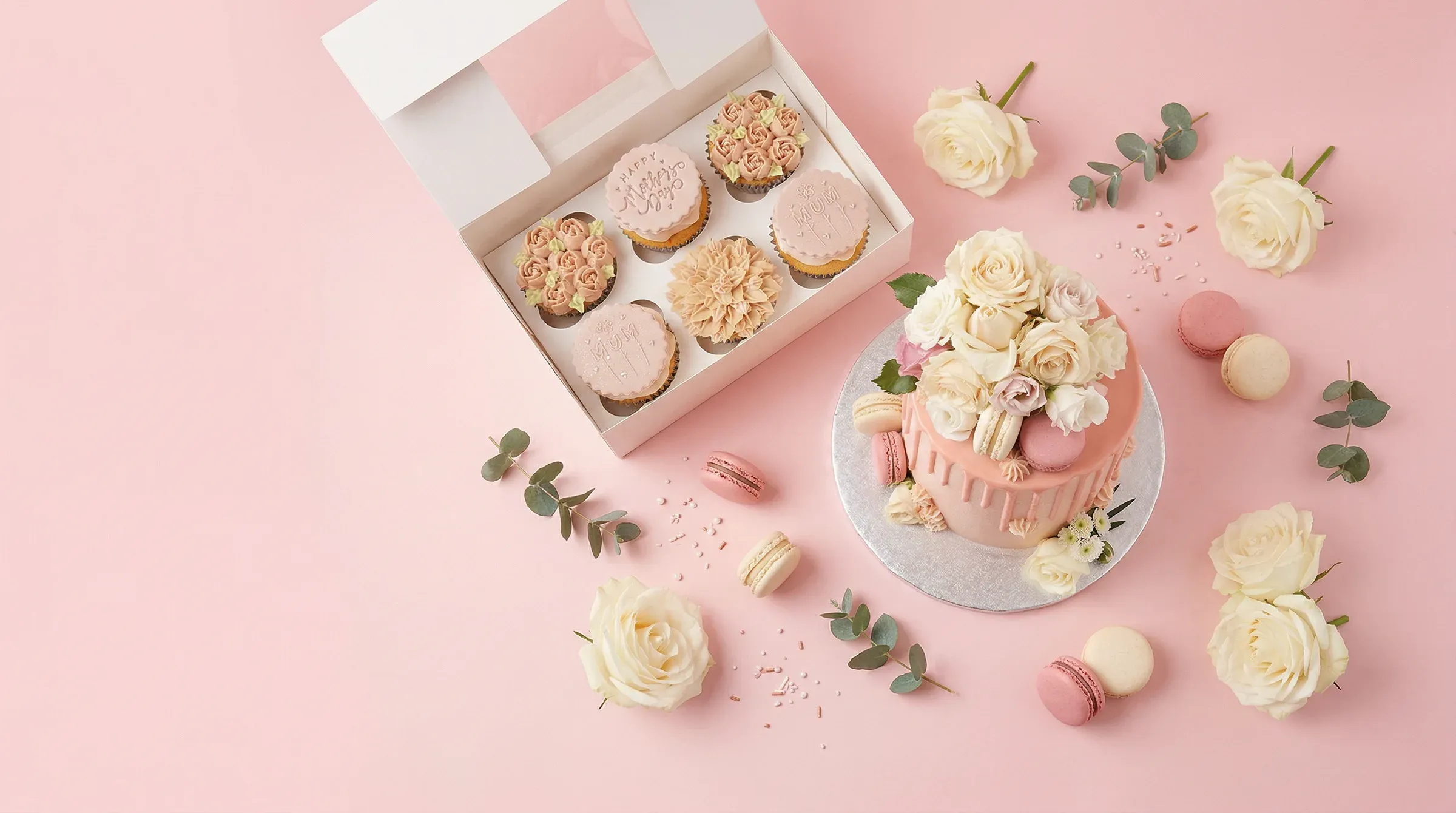 Flat-lay of Beth's handcrafted cakes, cupcakes, and macarons on a blush pink background