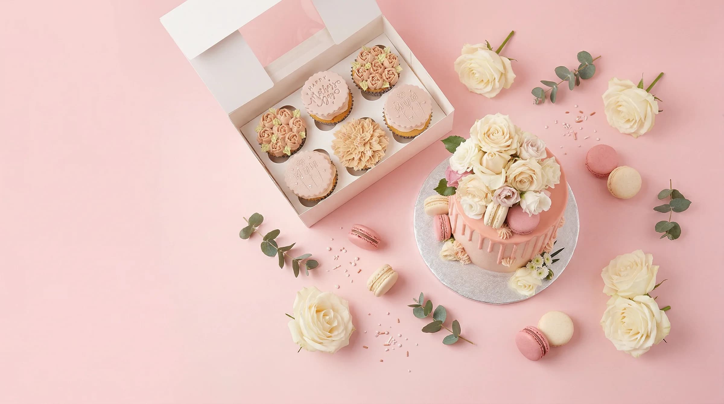 Flat-lay of Beth's handcrafted cakes, cupcakes, and macarons on a blush pink background