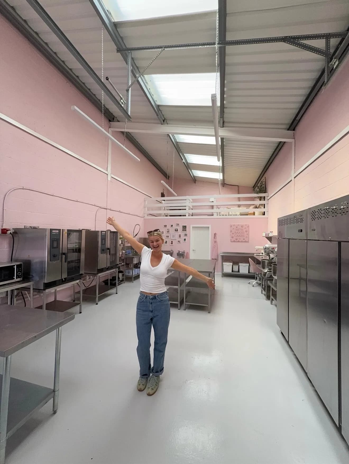 Beth with arms outstretched in her new pink commercial kitchen and HQ